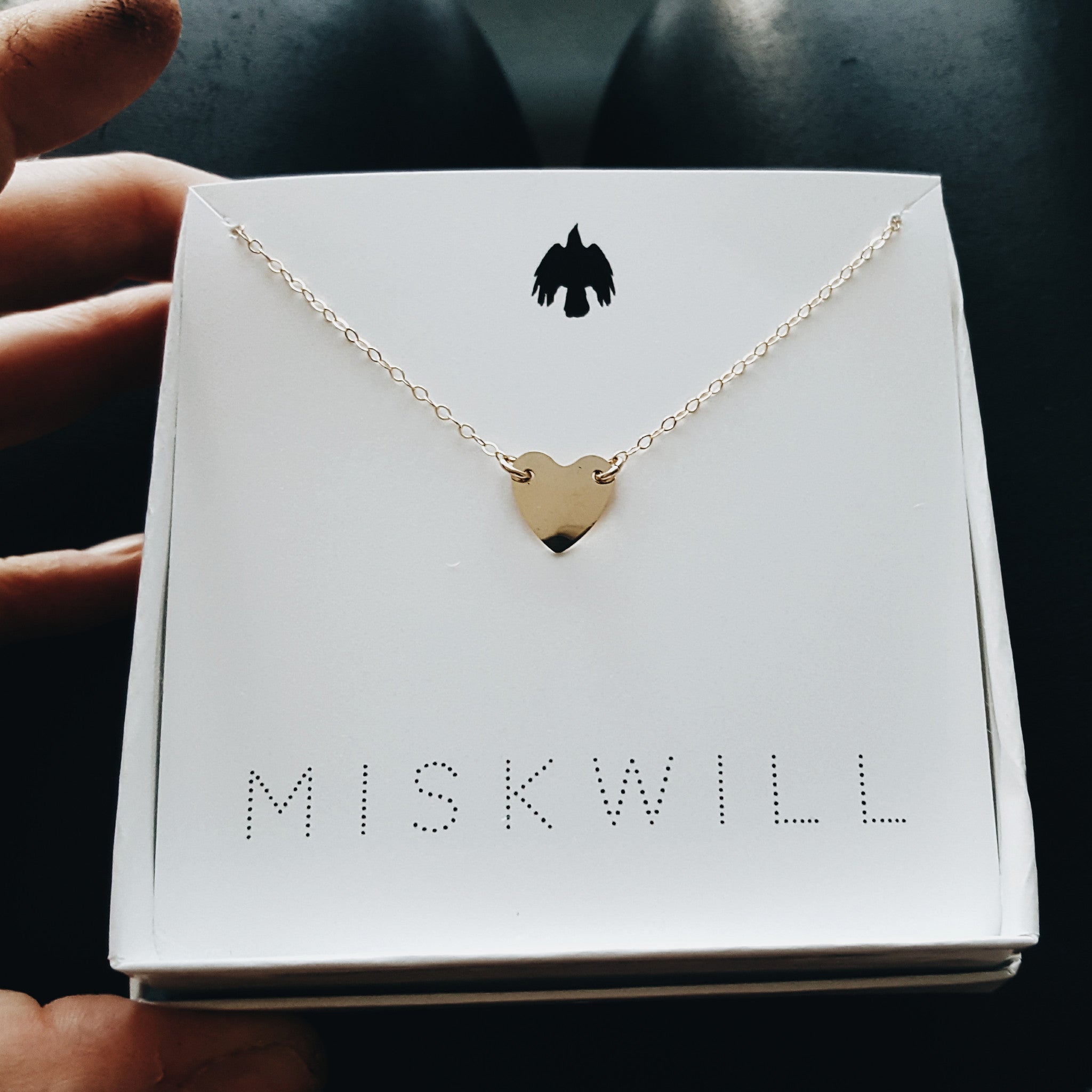 a small gold heart shaped pendant on a gold chain displayed in a small white jewelry box