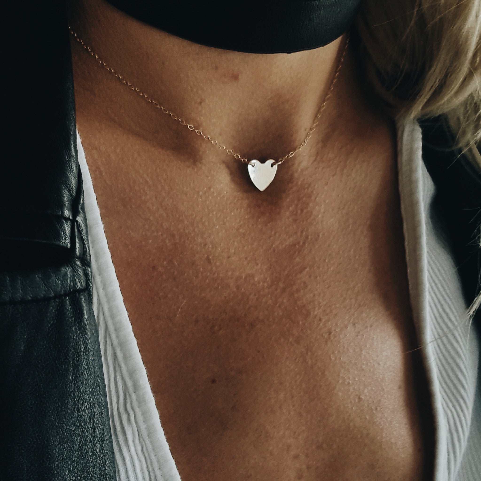 a close up of a woman's neck wearing a gold chain chocker with a small heart pendant and thick black choker