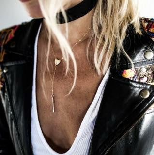 a close up of a woman in a white shirt and black biker jacket wearing a gold heart lariat necklace and thick black chocker style necklace