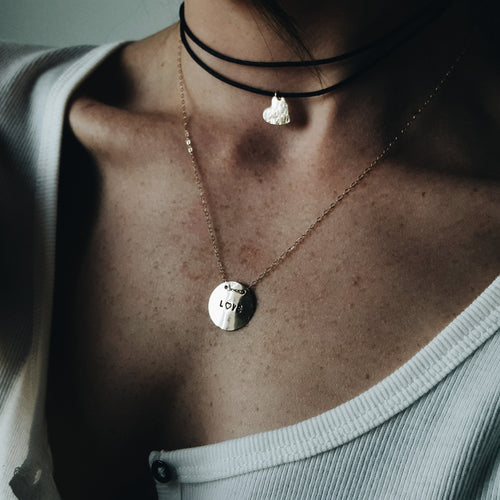 a close up of a woman's neck with a black wrapped chocker and a gold pendant with love stamped on it 