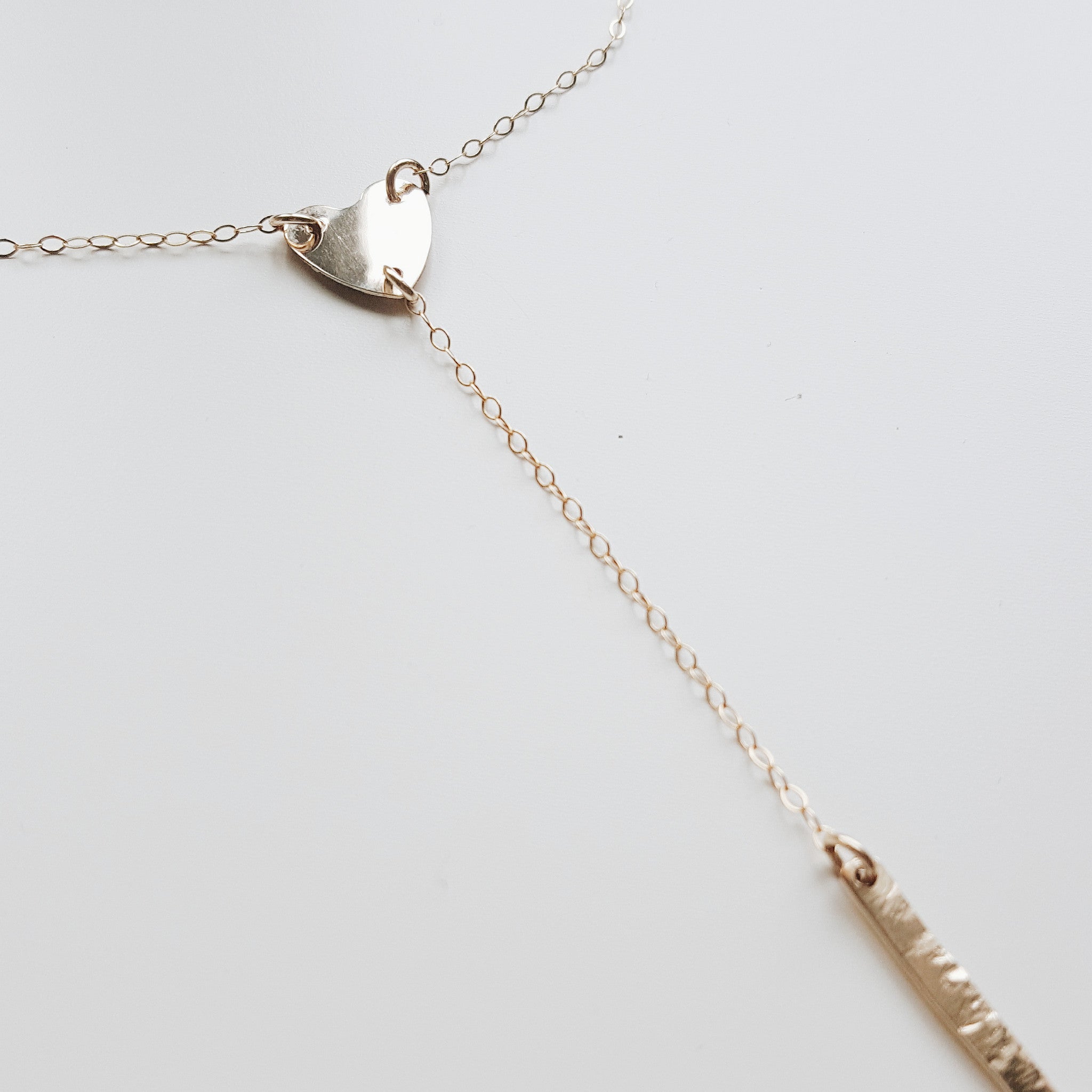 a gold heart lariat necklace with gold chain and a simple gold bar on a white background