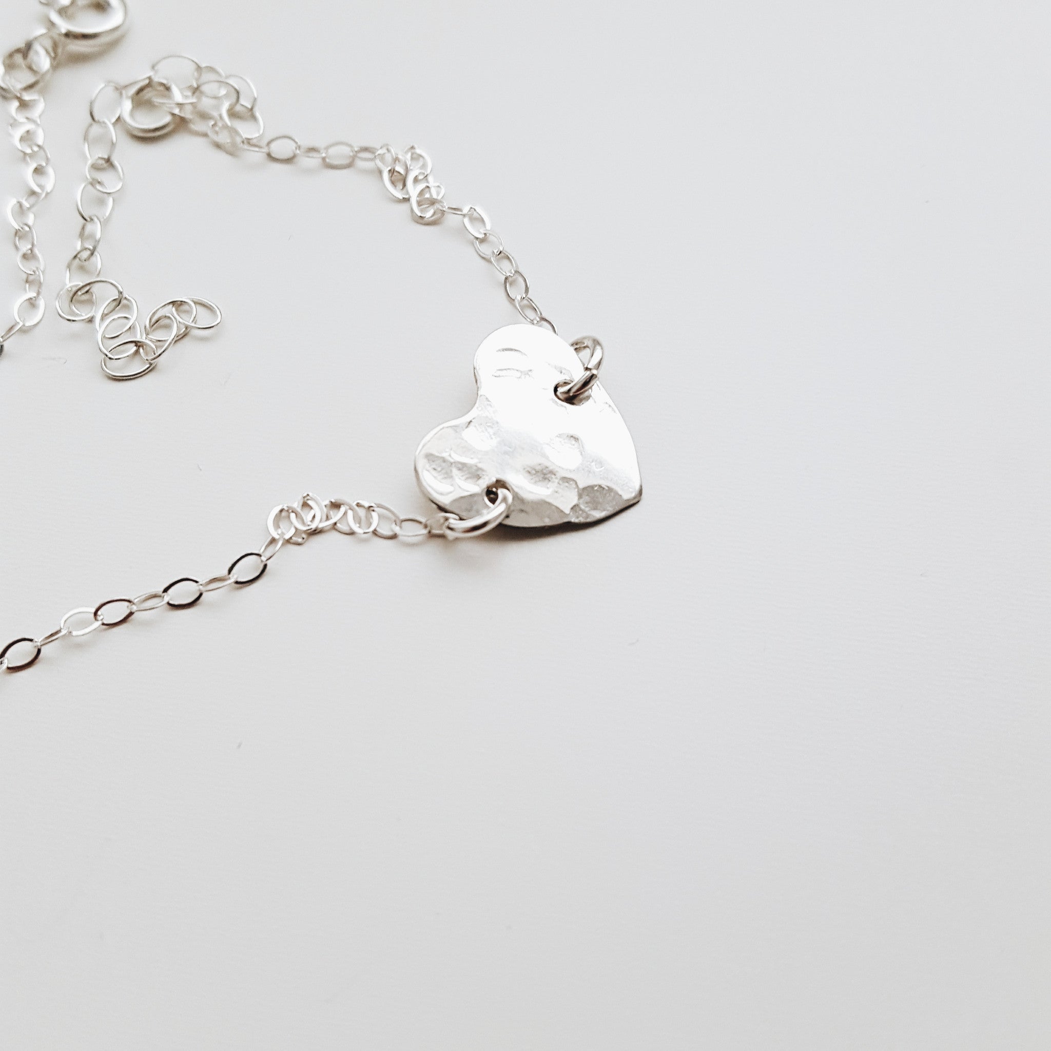 a small silver hammered heart pendant on a silver chain with a white backgroud