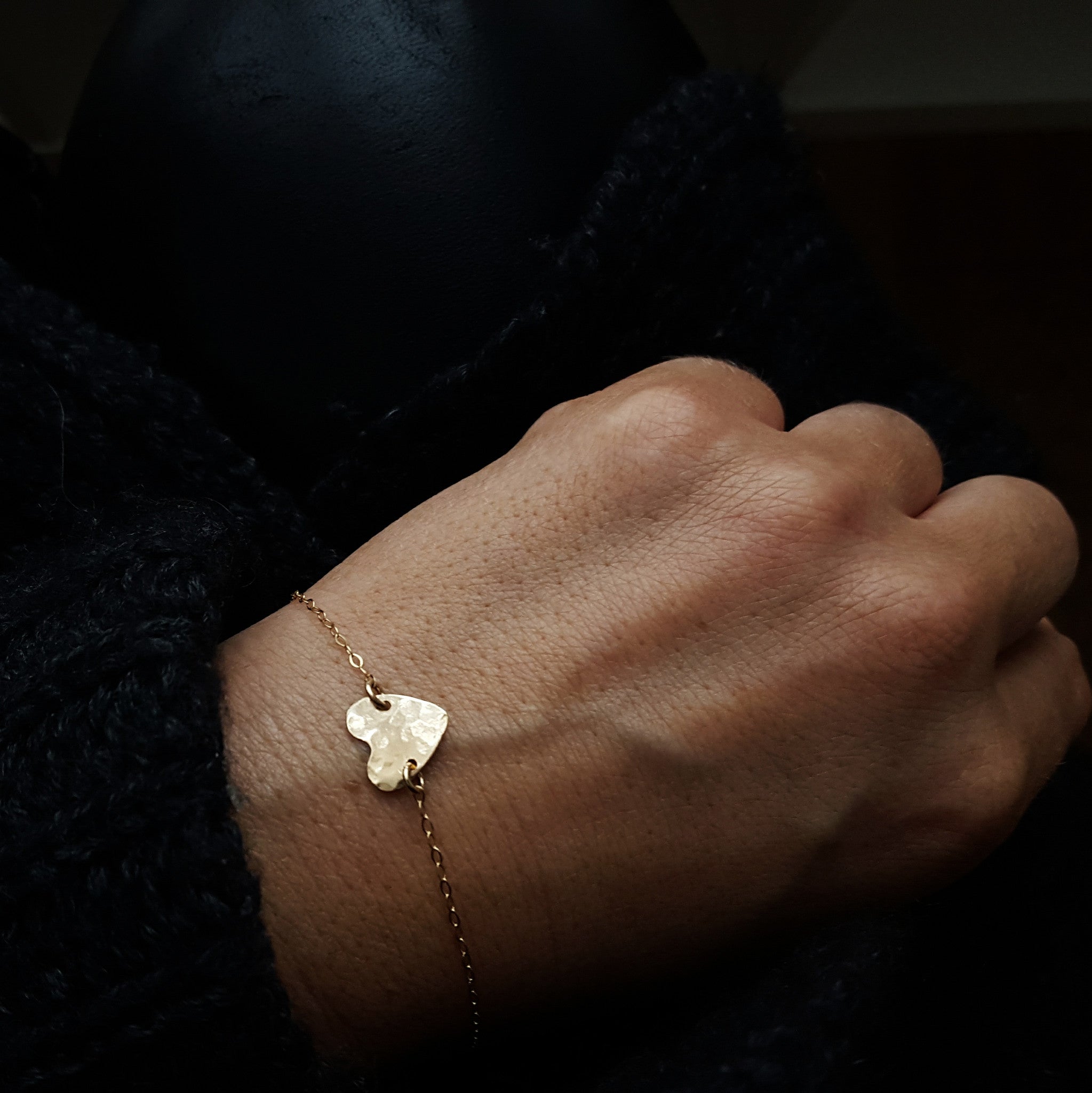 a close up of a wrist wearing a small chain bracelet connected by a small gold hammered heart pendant