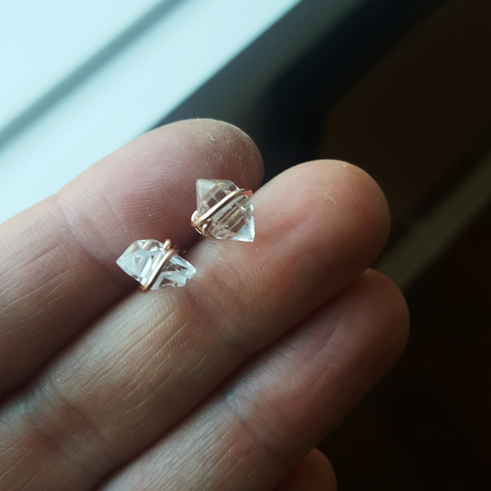 a pair of gold herkimer diamond earrings held between two fingers