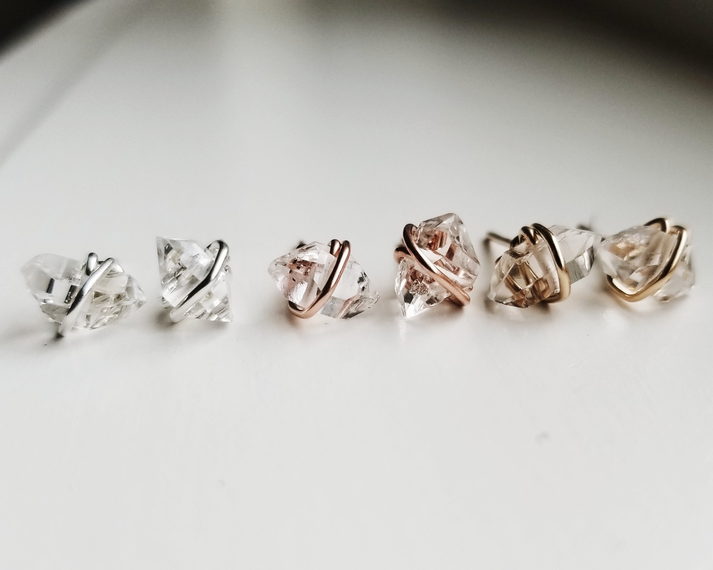 a trio of sets of herkimer diamond earrings in silver, rose gold and gold on a white background