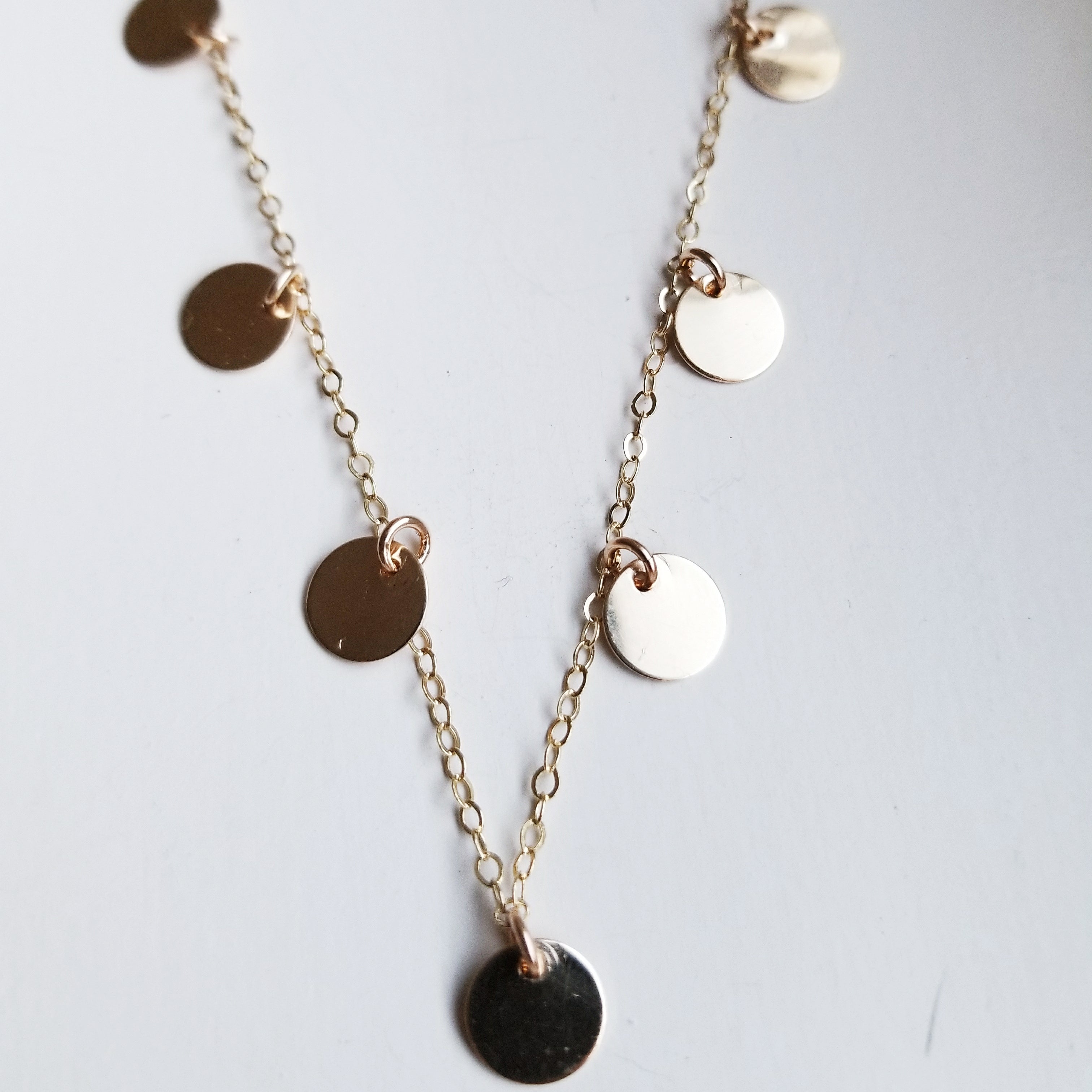 a gold necklace with small dangling gold circle pendants on a white background