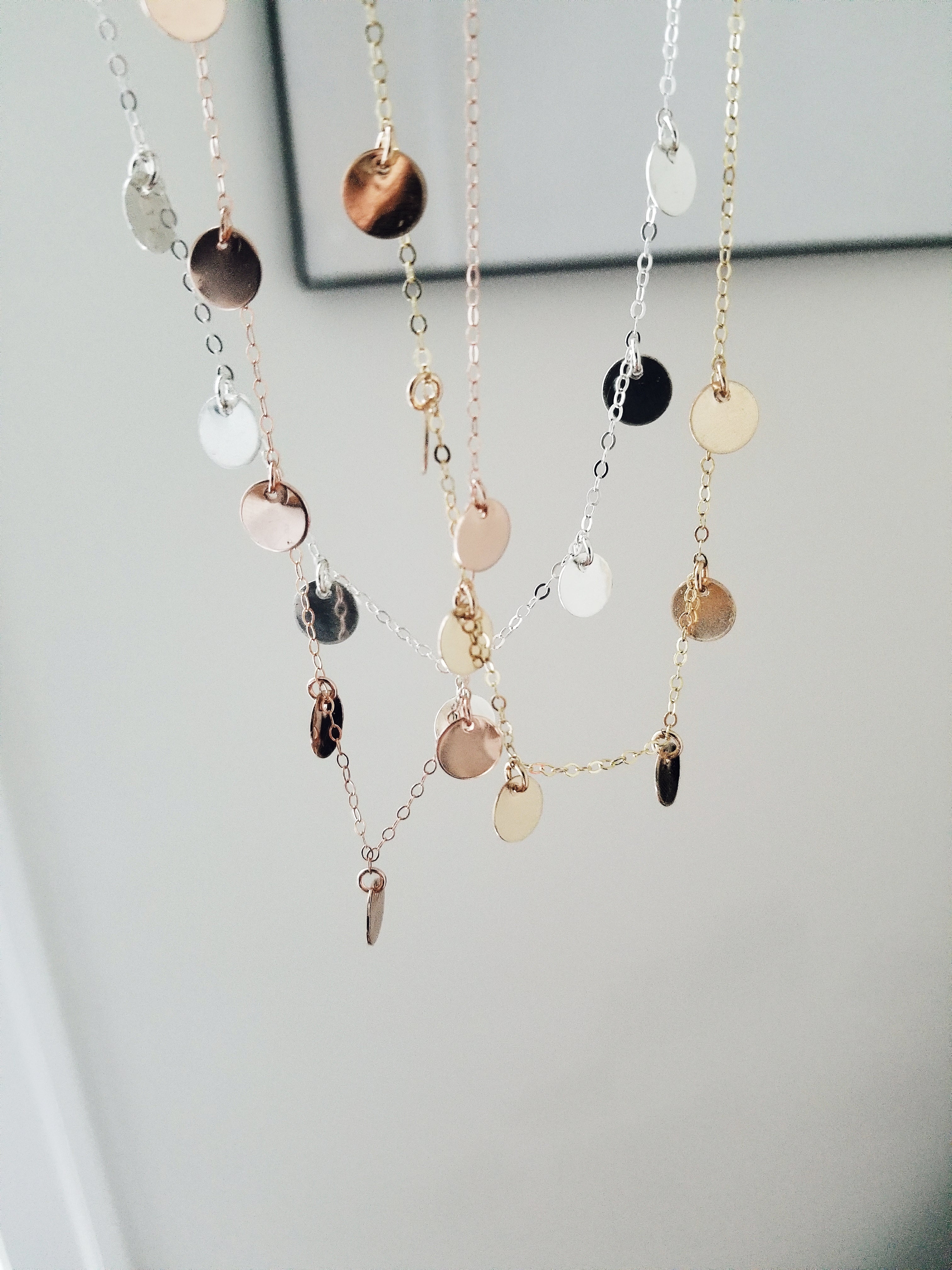 a hanging group of little luna necklaces in gold, silver and rose gold in front of a white background