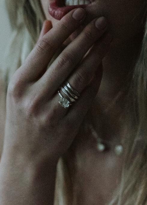 close up of a blonde girl wearing three stacked silver rings and a herkimer diamond ring on her finger near her mouth