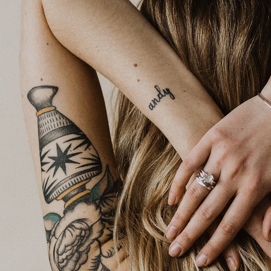 a back view of a woman's tattooed arm behind her head wearing a gold ring and a herkimer diamond ring on one finger