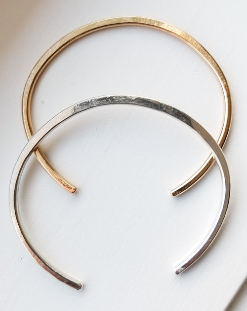 two cuff bracelts, one gold and one silver on a white background
