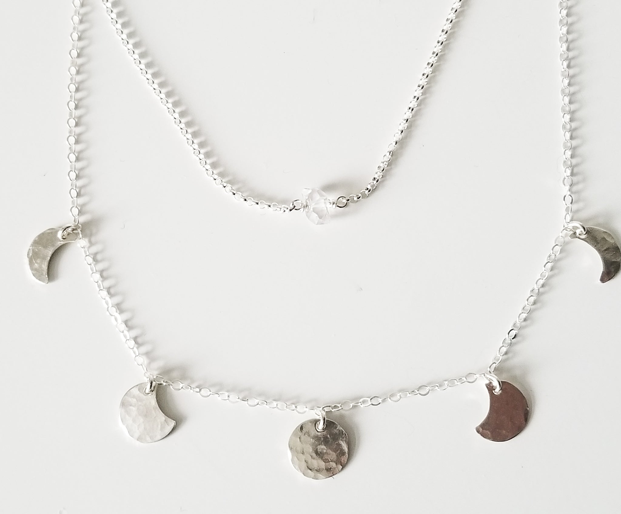 a silver chain necklace with small moon pendants showing the moon phase and a small herkimer diamond on a silver chain with a white background