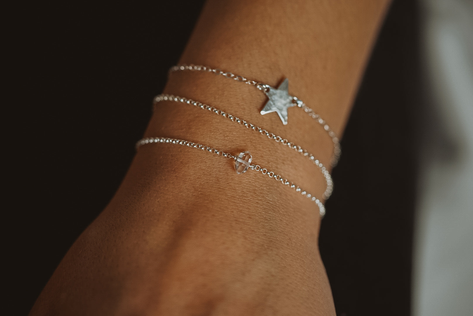 a close up of a wrist wearing a silver chain bracelet, a silver star pendant bracelet and small herkimer diamond bracelet