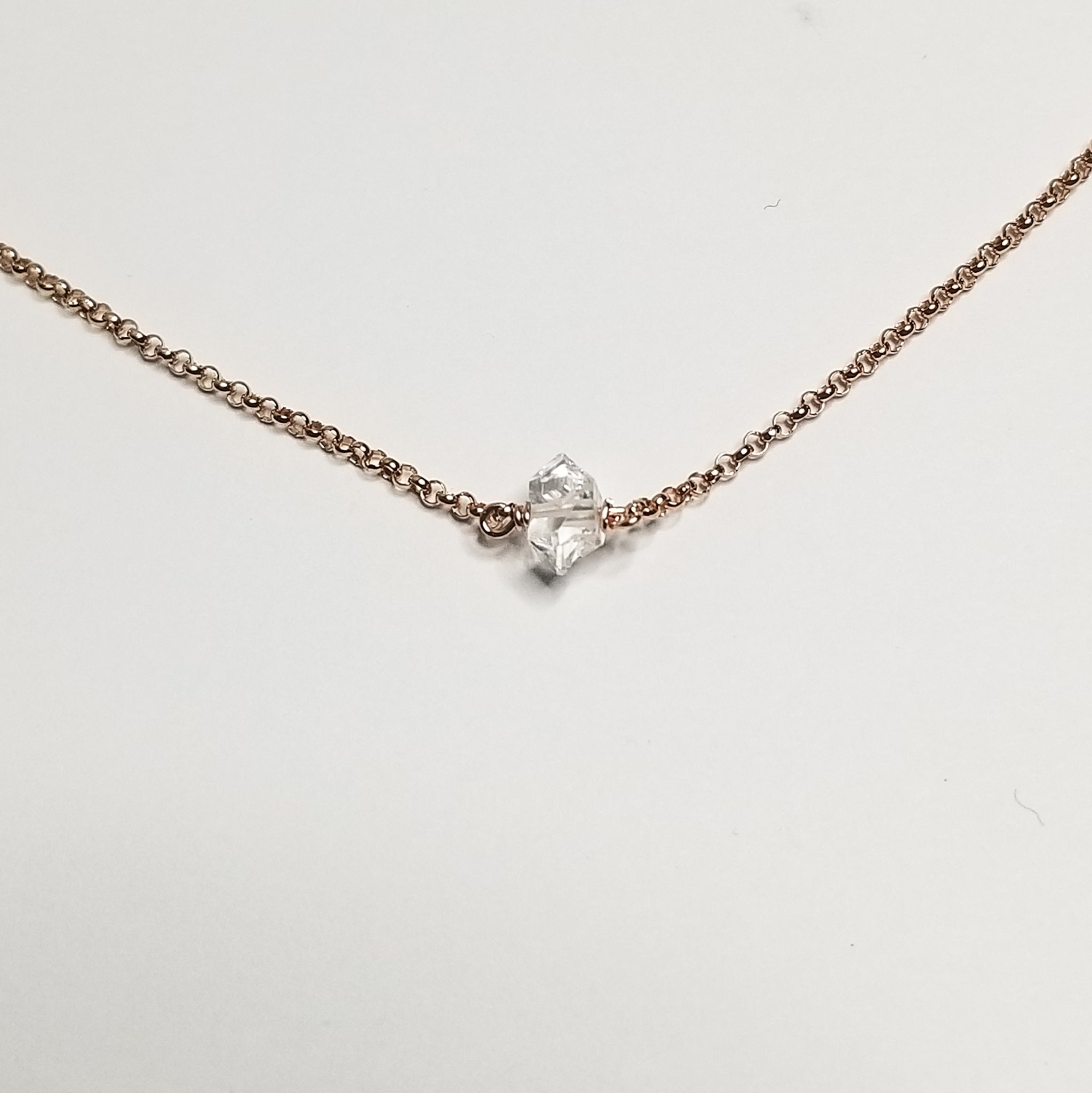 a herkimer diamond on rose gold chain with a white background