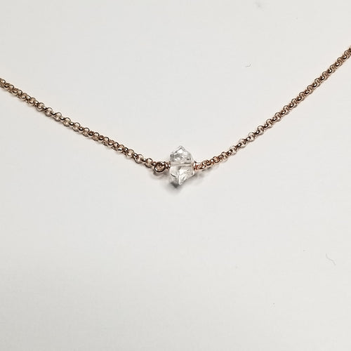 a herkimer diamond on rose gold chain with a white background