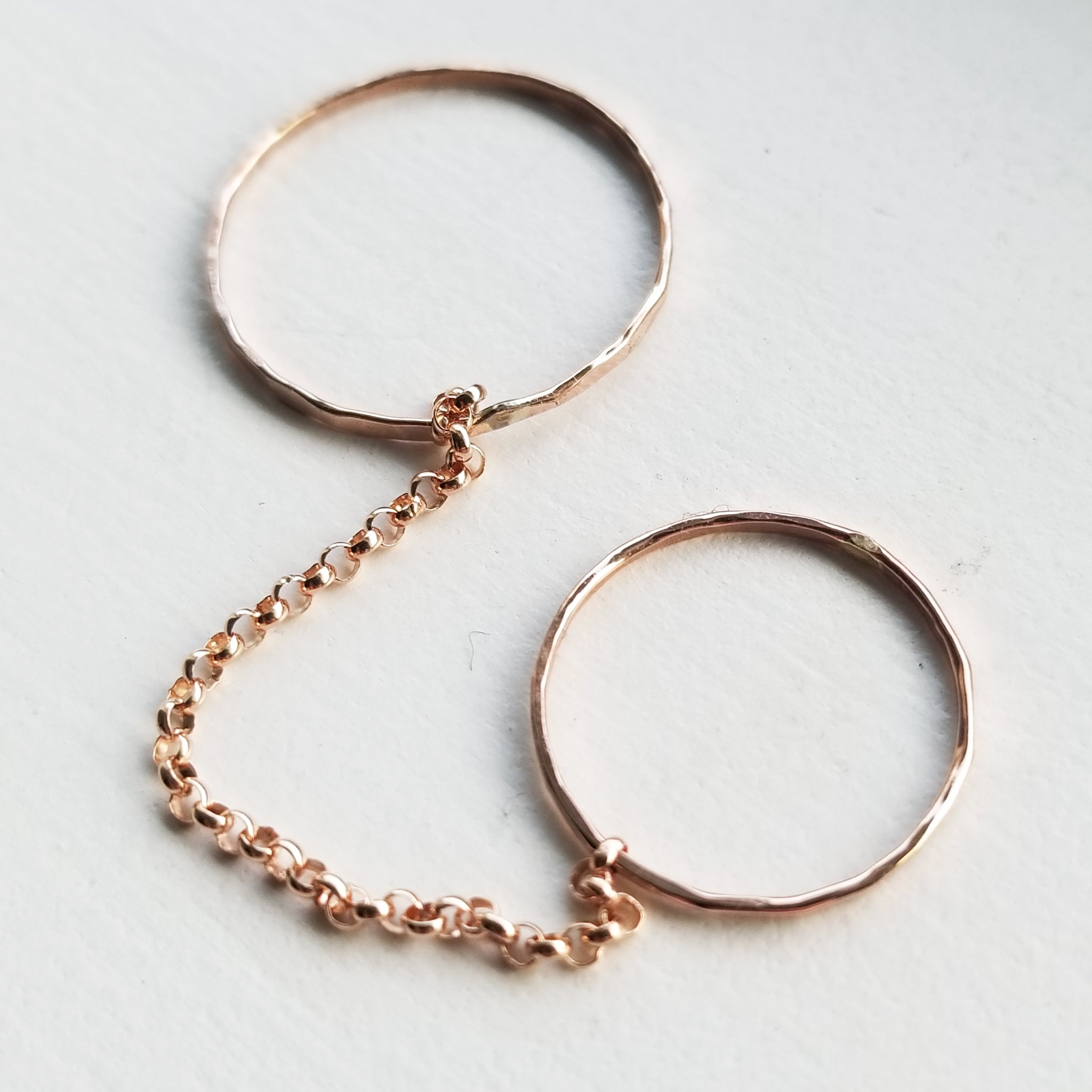 a set of two rose gold simple band rings connected by a rose gold chain on a white background