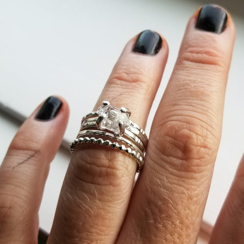 a close up of a hand with black painted nails wearing a stack of silver rings