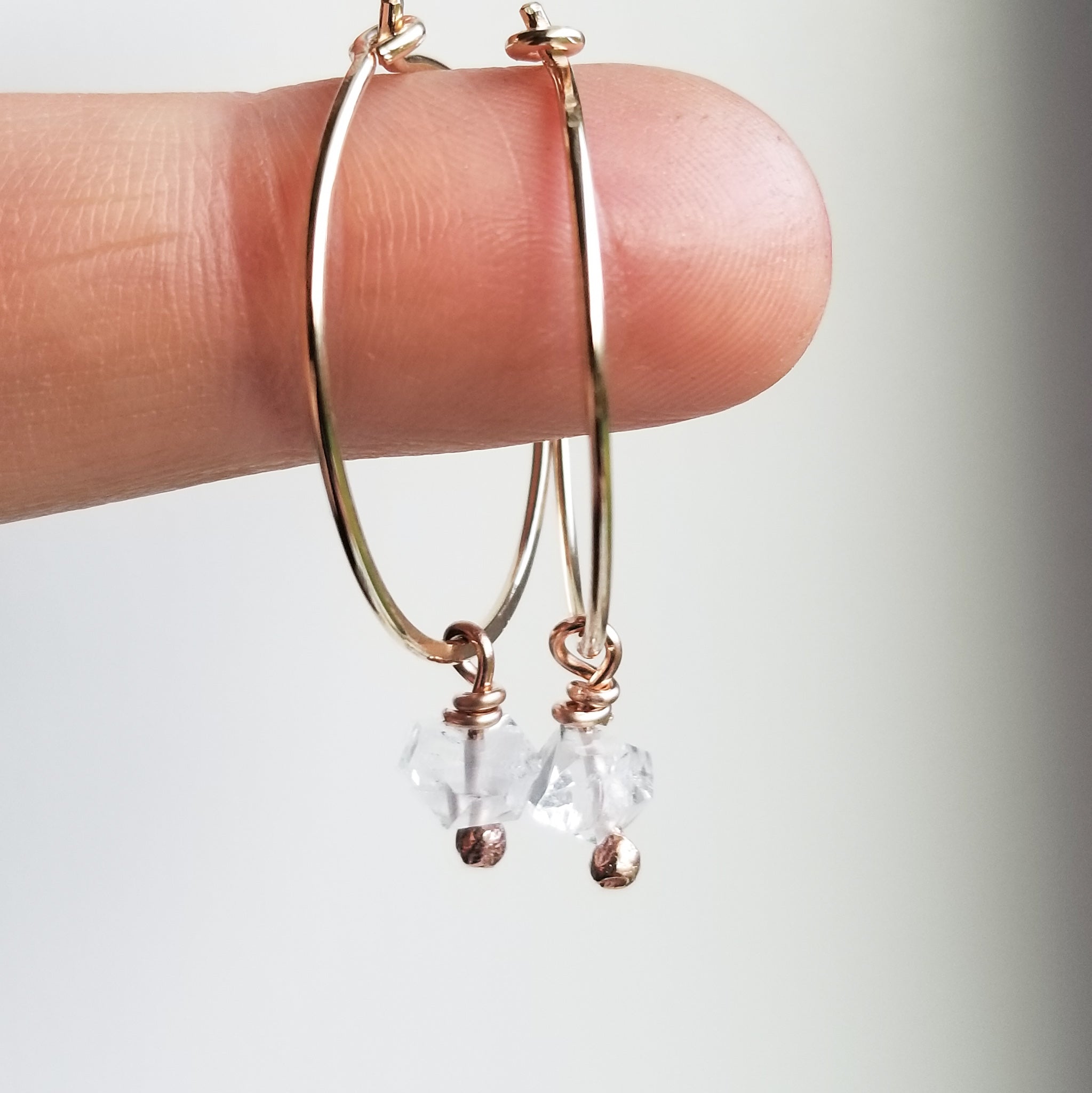 a finger holding small gold hoop earrings with herkimer diamonds dangling off on white background