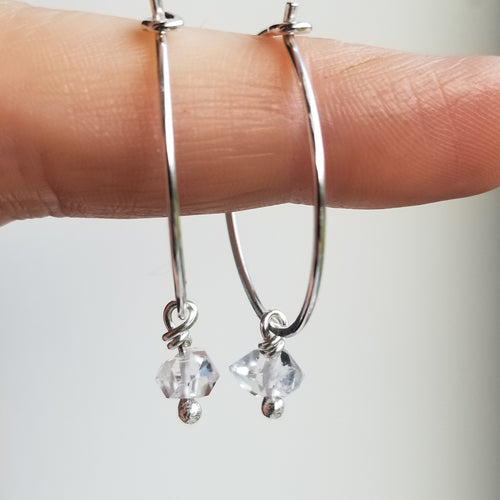 a finger holding small silver hoop earrings with herkimer diamonds