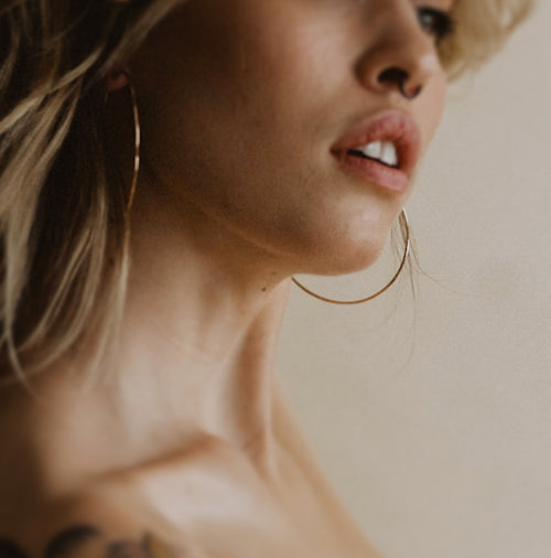 a close up of a model wearing large gold hoop earrings and a white background