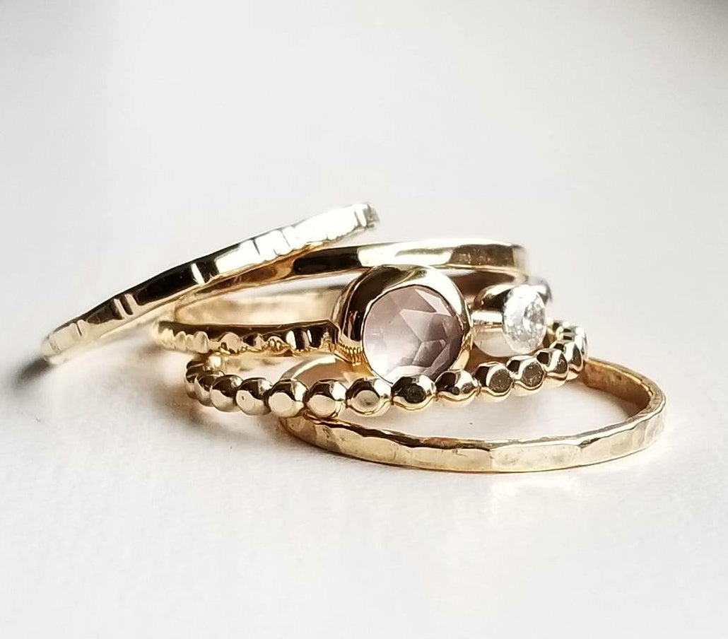 a stack of different varieties of gold rings, including a round double diamond ring in the centre on a white background