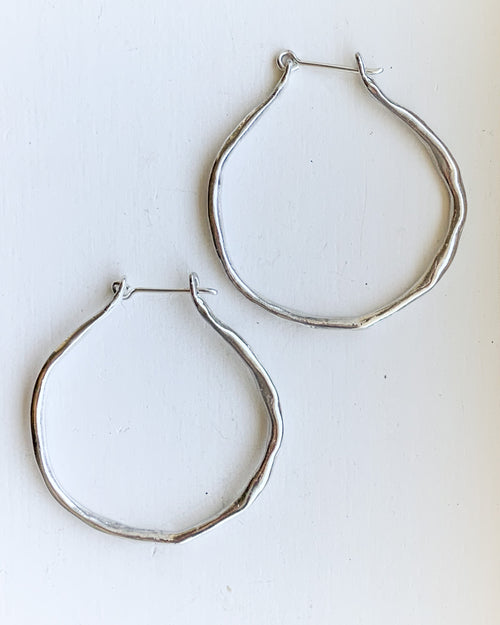 a set of hand formed silver hoop earrings shown on a white background