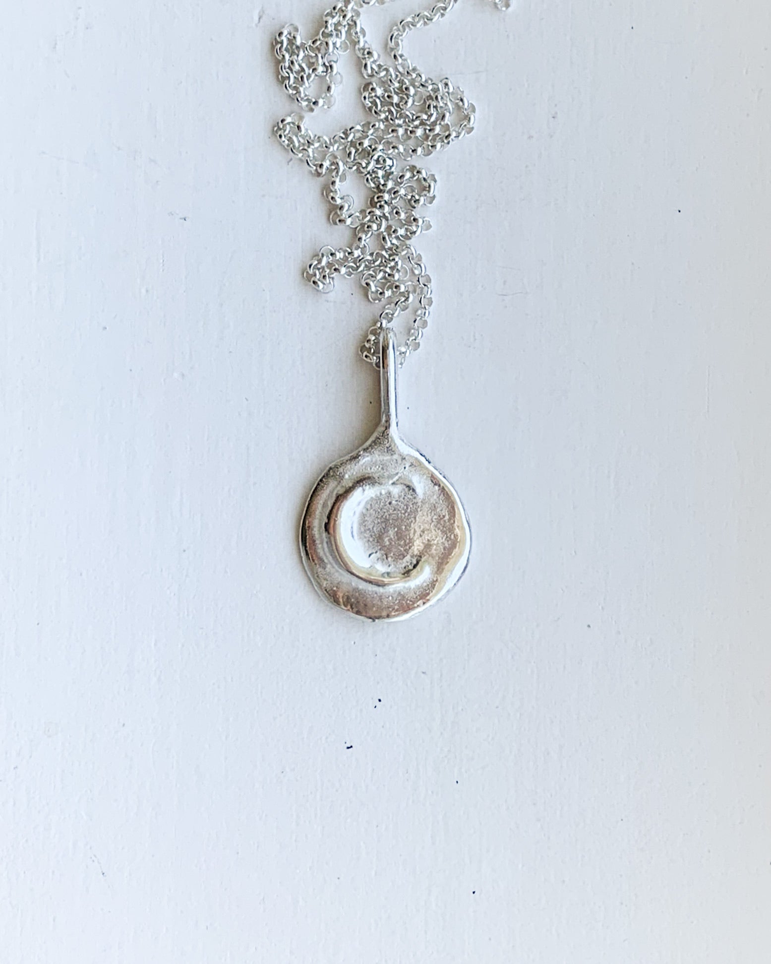 a hand sculpted silver moon pendant on a silver chain with a white background