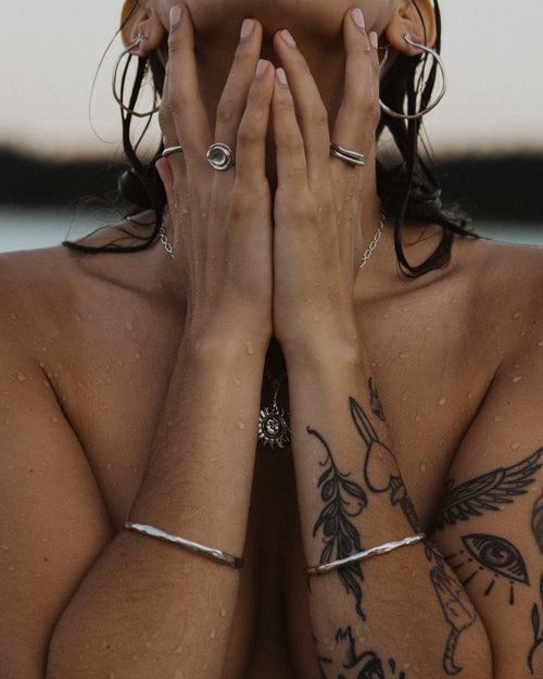 a woman holding her hands in front of her face, loaded with silver jewelry and wet from the beach