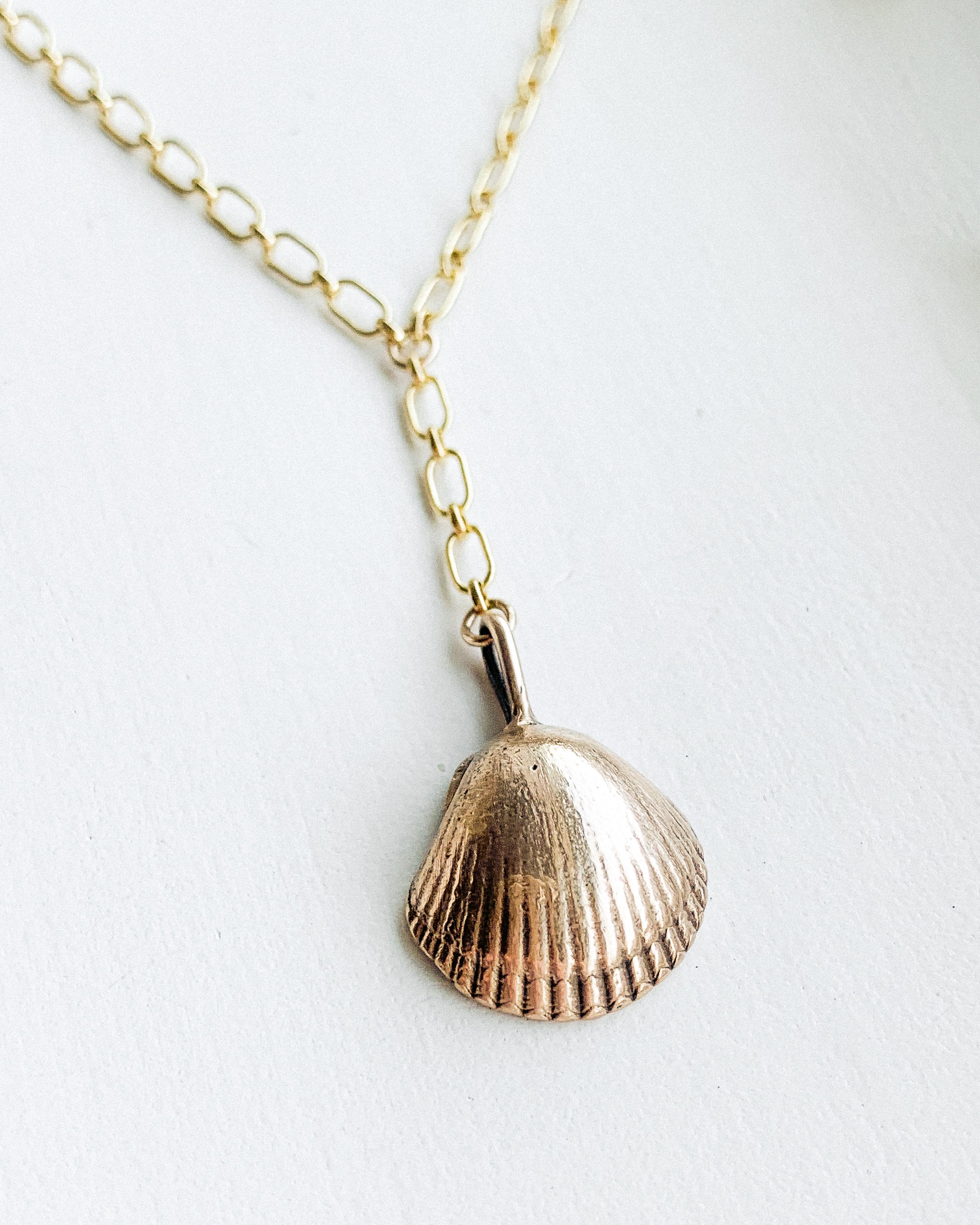 a bronze sea shell pendant on a gold lariat chain, shown on a white background