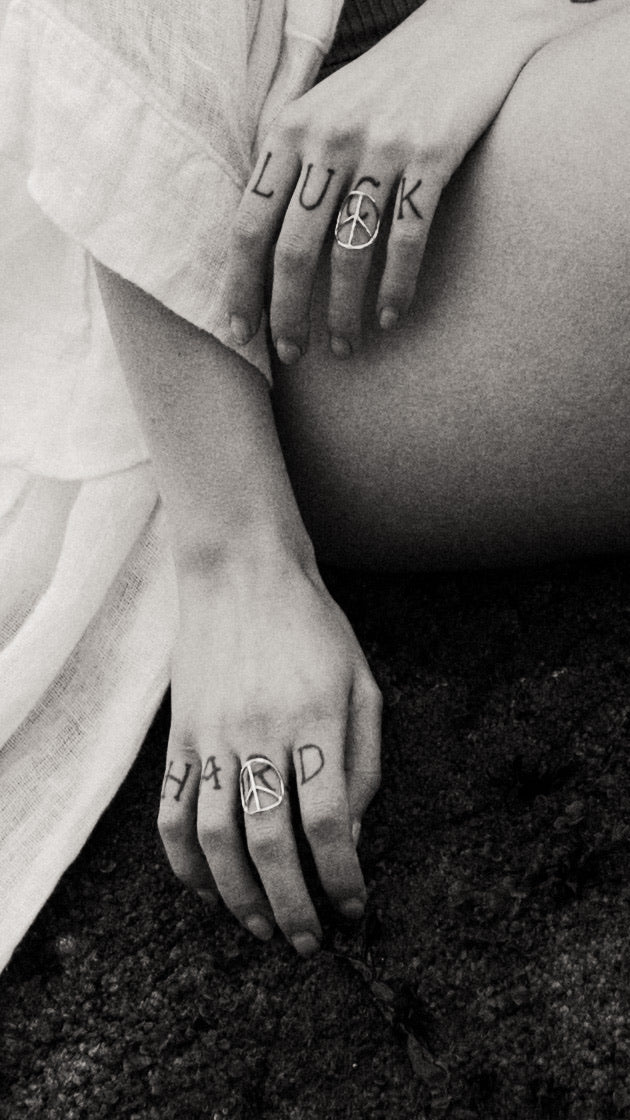 a black and white close up of two hands with tattooed fingers wearing two peace sign shaped rings 