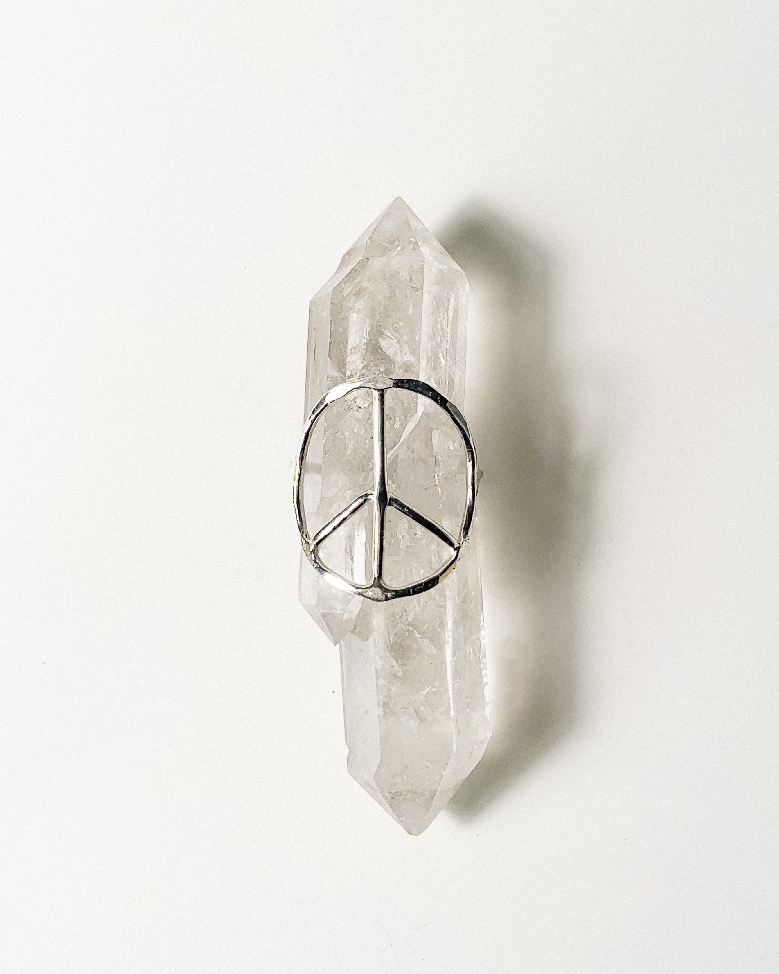 a silver peace sign shaped ring displayed on a crystal with a white background