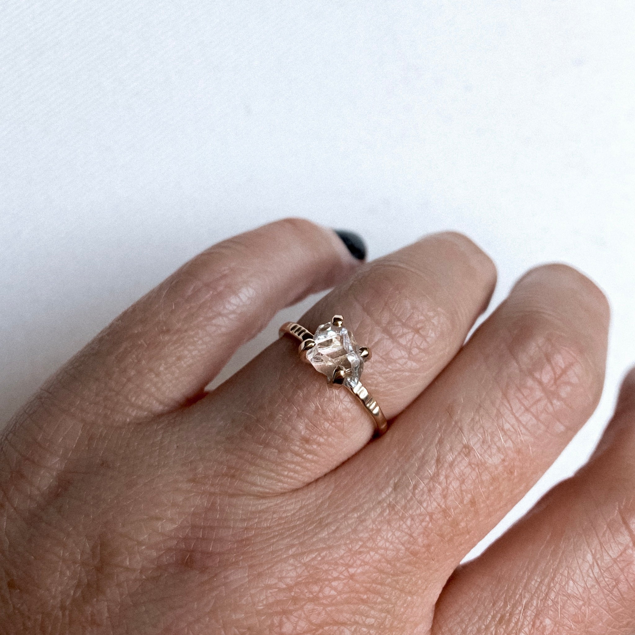 a close up of a finger wearing a gold claw style ring with a herkimer diamond