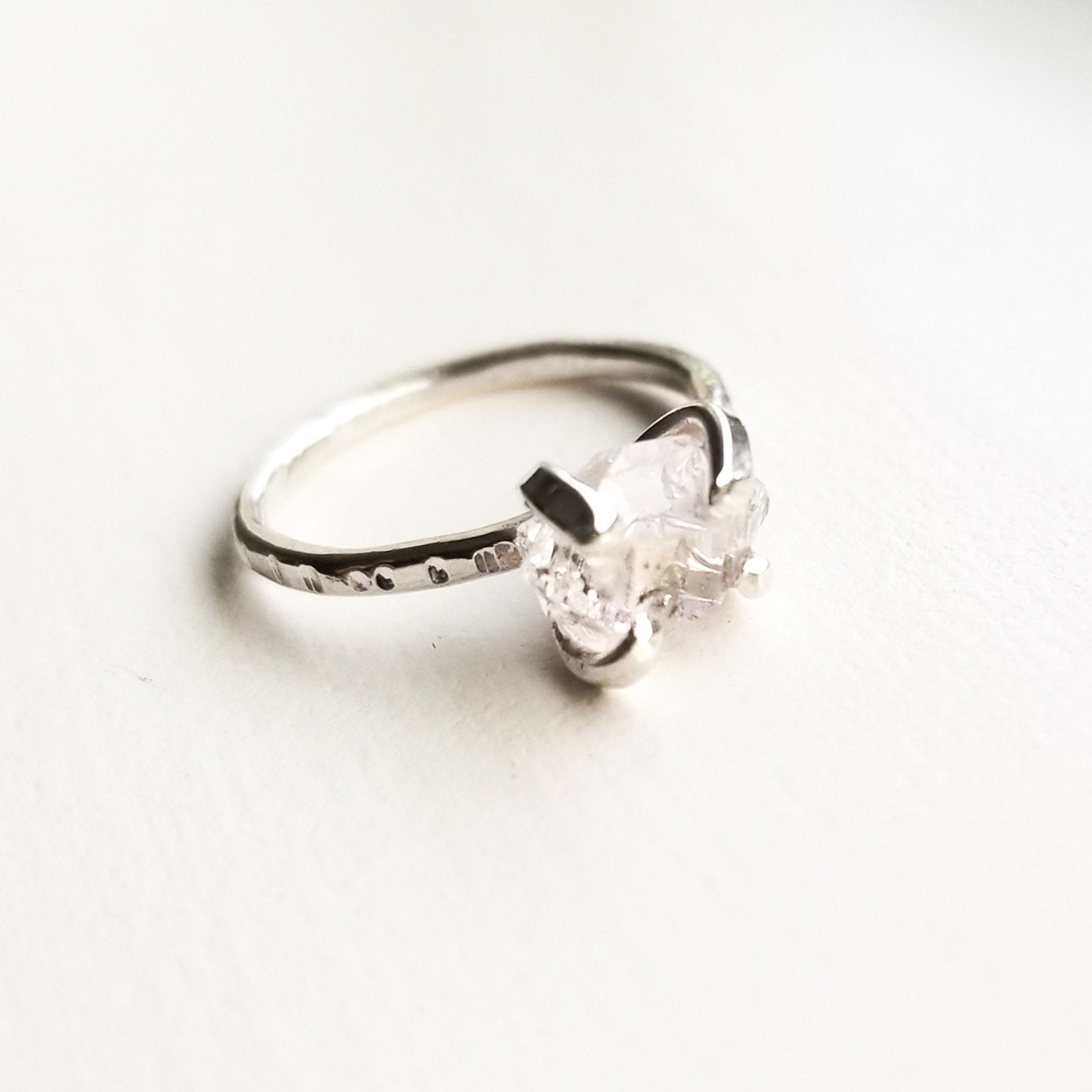 a silver claw style ring with a herkimer diamond on a white background