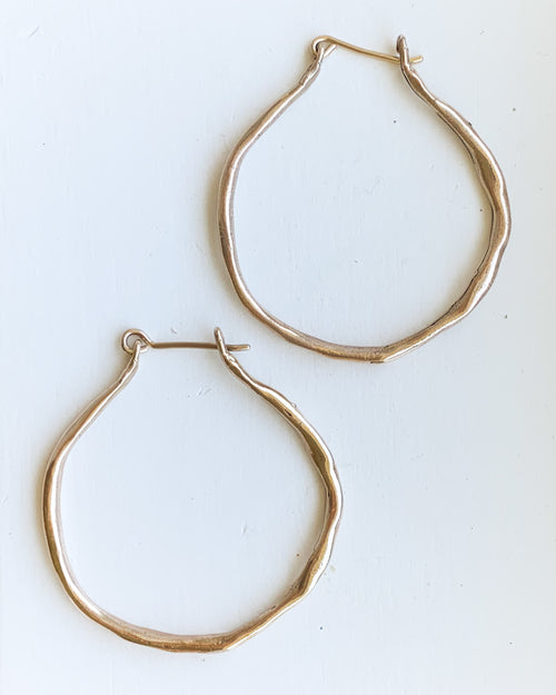 a set of hand formed gold hoop earrings shown on a white background