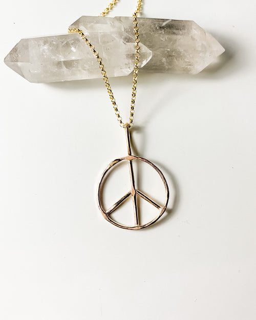 a gold peace sign pendant necklace on a gold chain, shown on a white background and two quartz crystals