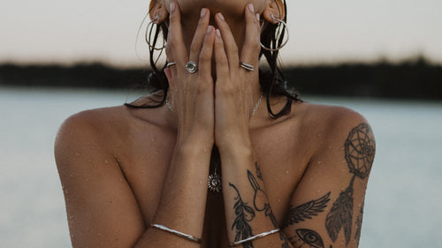 a close up of a woman at the beach with silver and bronze jewelry wet from the water