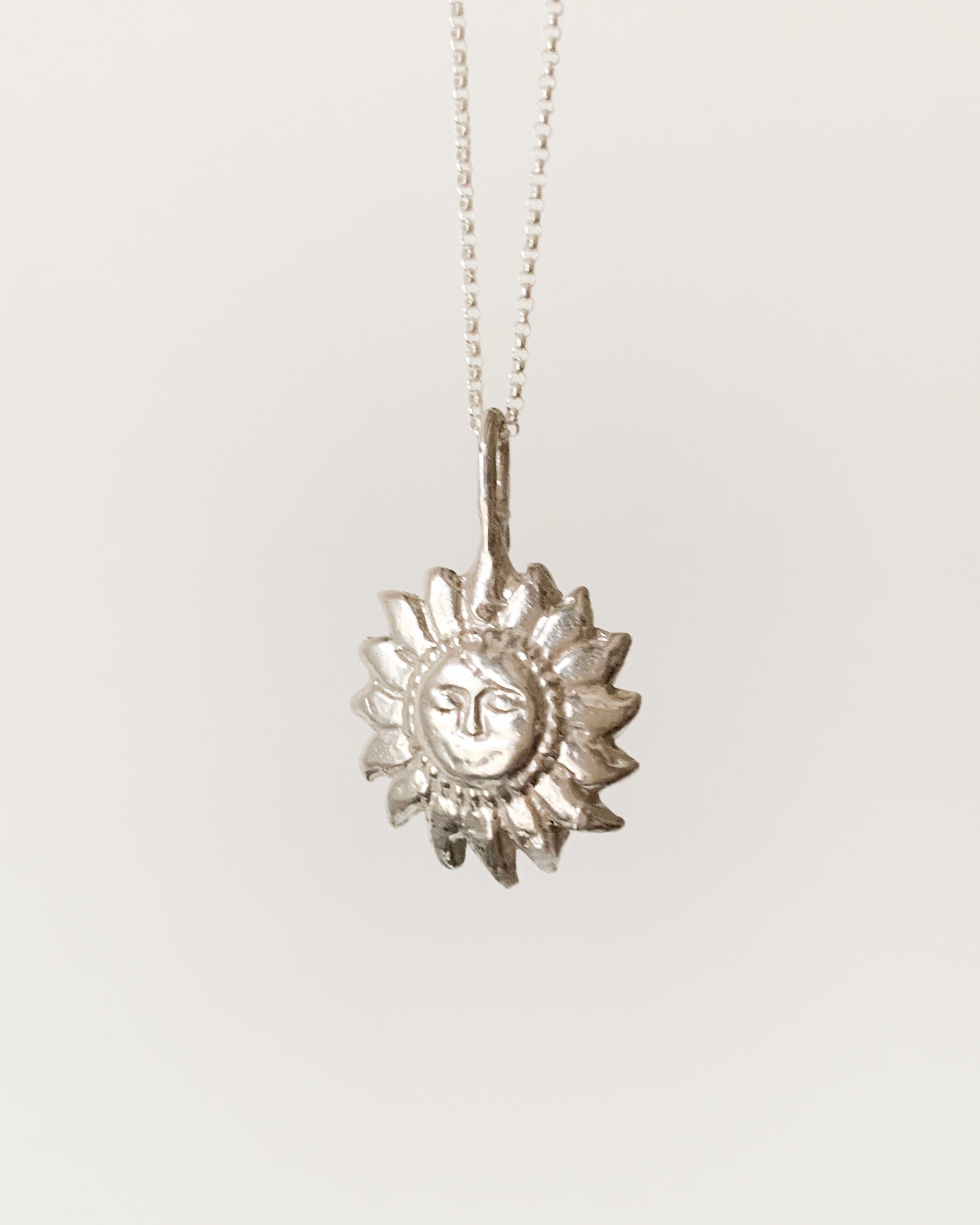 a silver sun shaped pendant necklace on a silver chain, shown on a white background