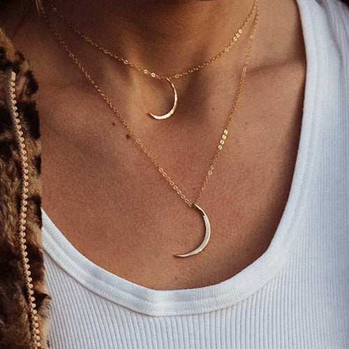 a close up of a woman wearing two gold crescent moon shaped pendant necklaces on gold chains and a white tank top
