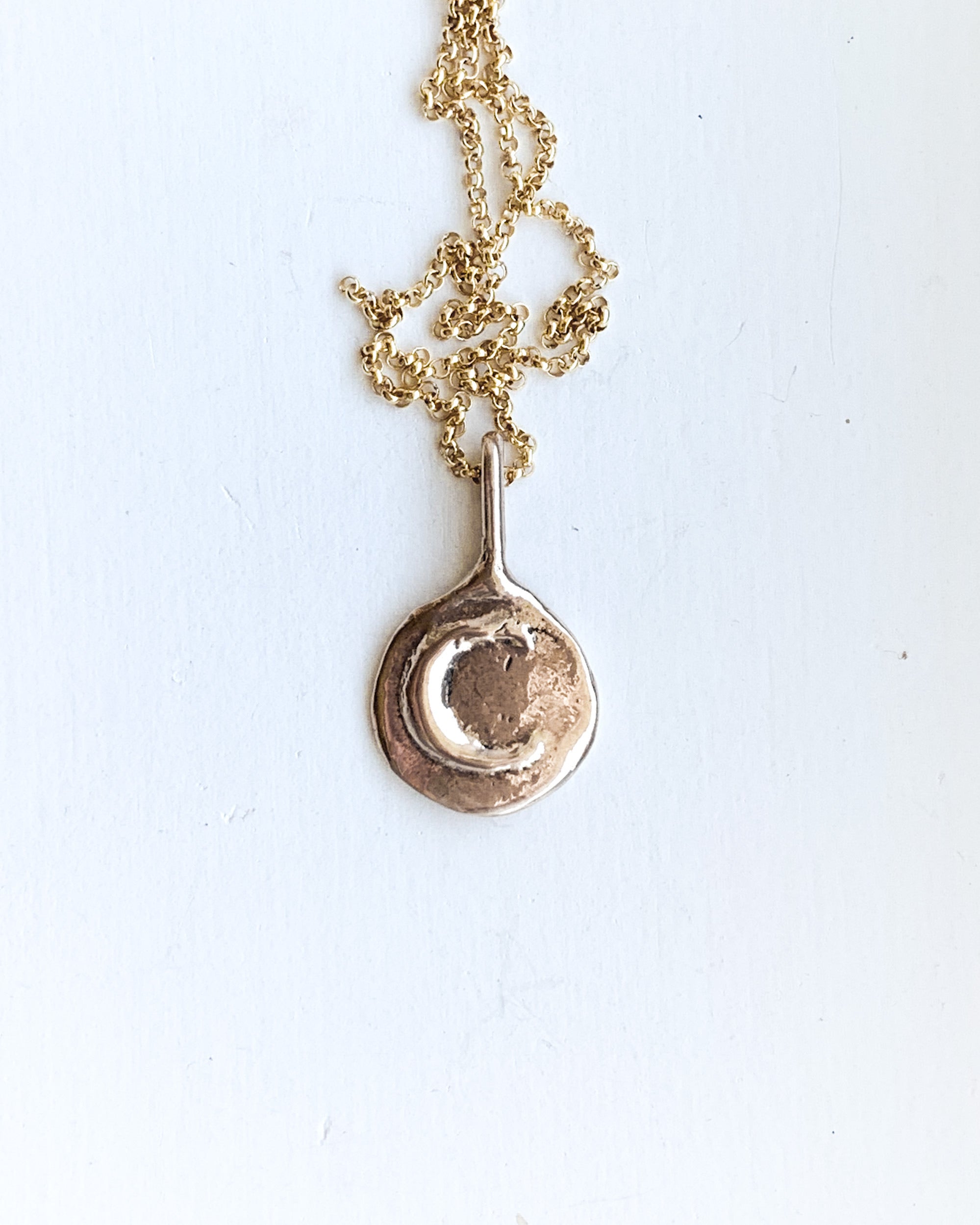a hand formed bronze moon pendant with a gold chain on a white backgroud