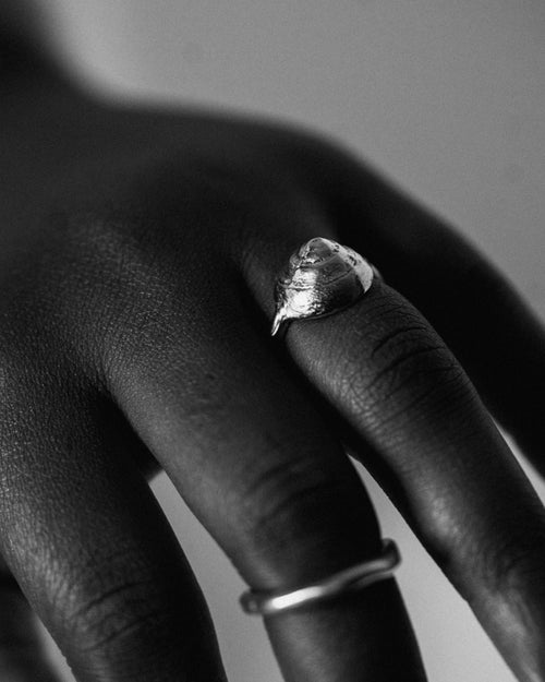 a black and white close up of a hand wearing a small silver sea shell ring and a simple silver band ring