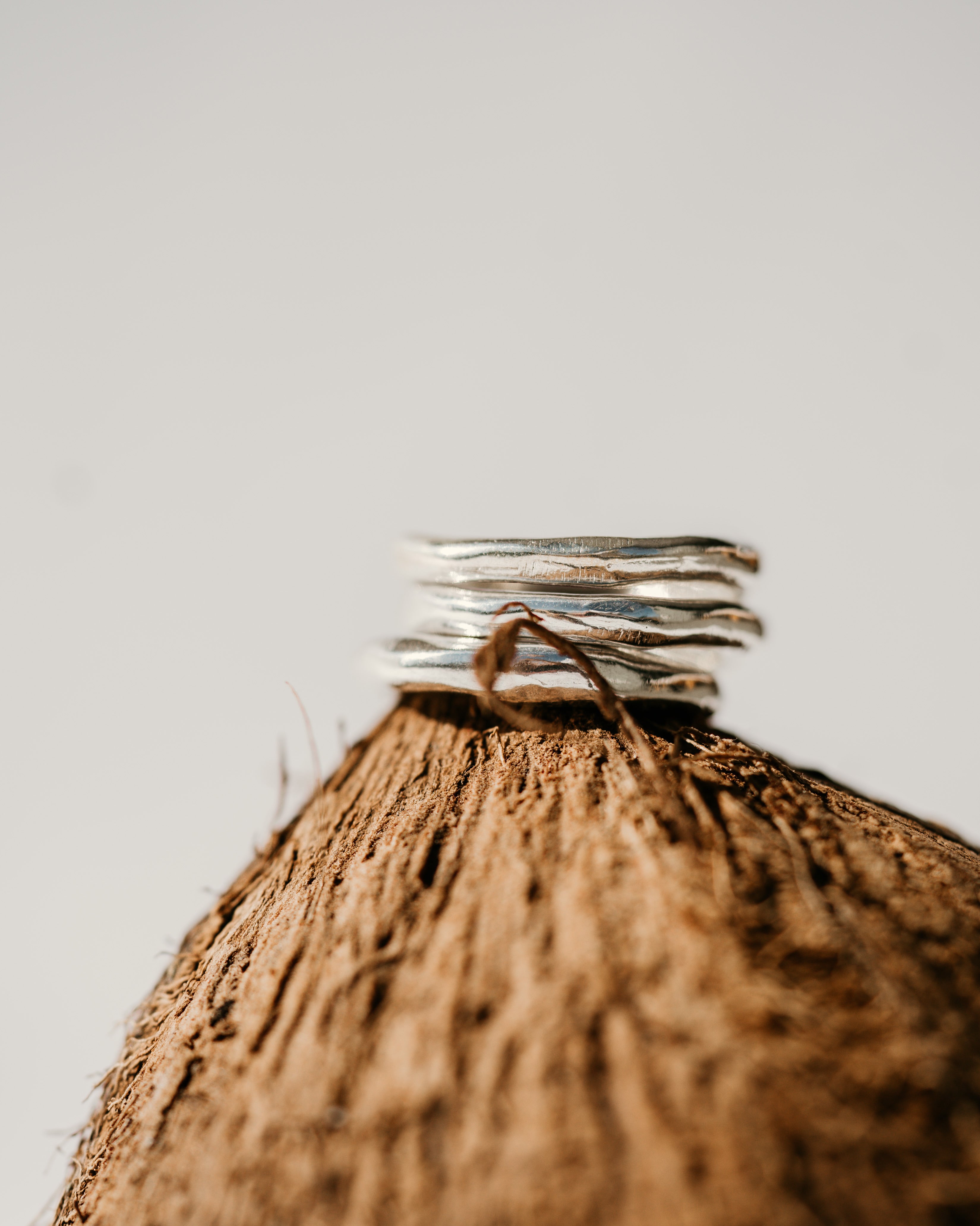 a stack of three hand formed silver band rings, balanced on top of a coconut with a white background 