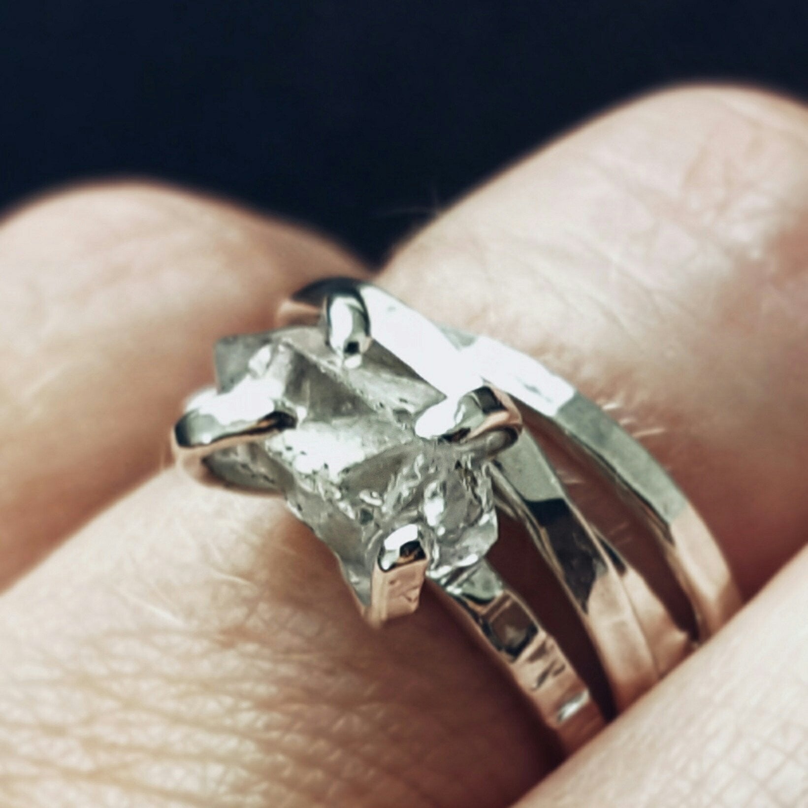 a close up of a finger wearing a set of intertwined silver bad rings and a silver claw style ring