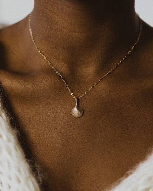 close up of a womans neck wearing a small bronze clamshell necklace and white knit sweater