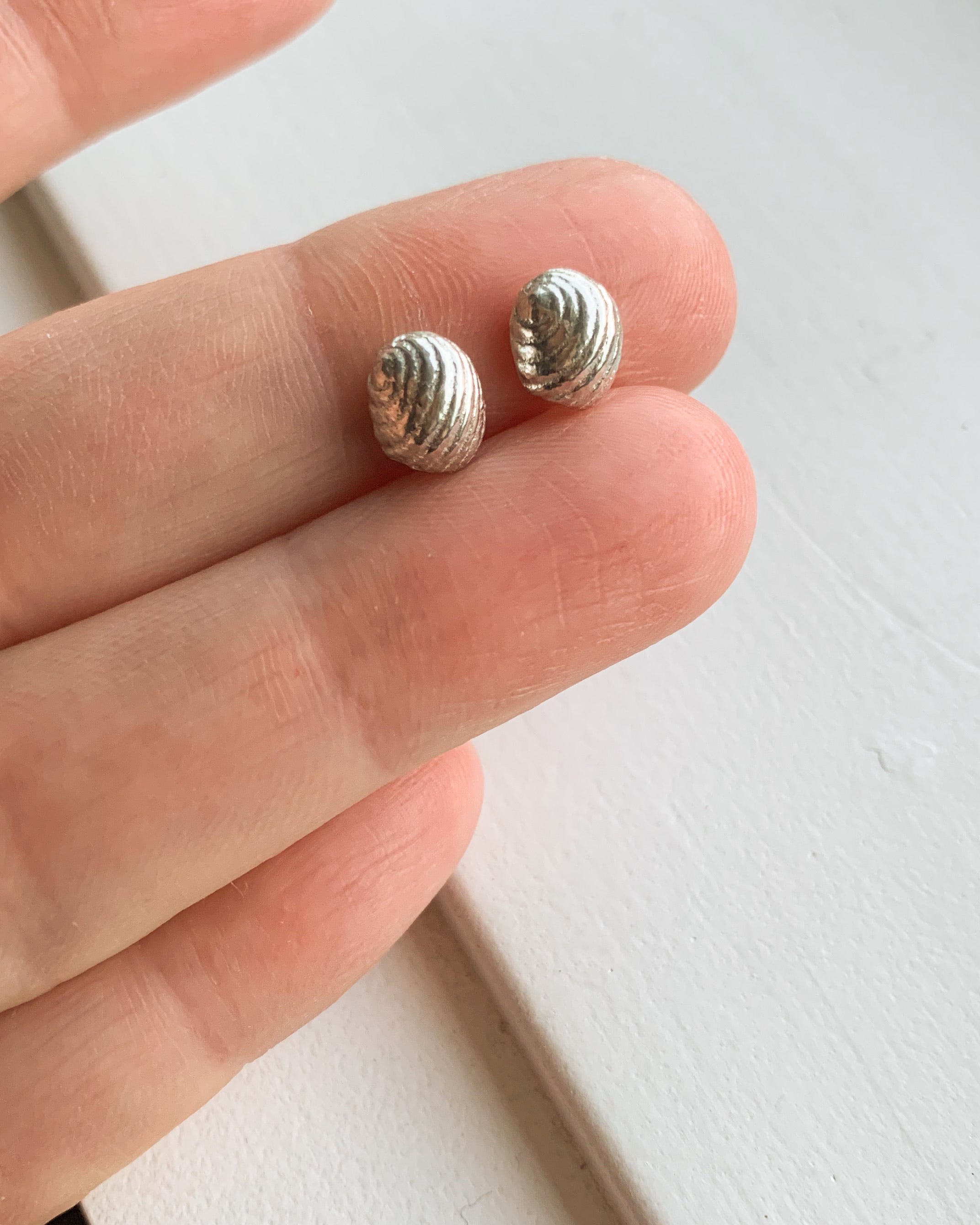 small silver sea shell stud earrings held between two fingers