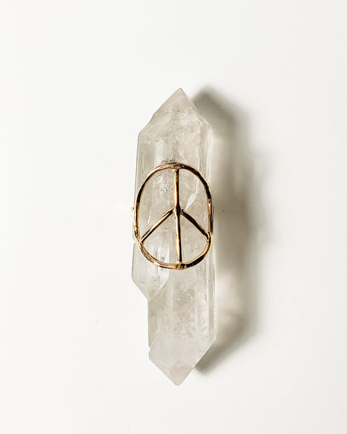 a gold peace sign shaped ring displayed on a crystal with a white background