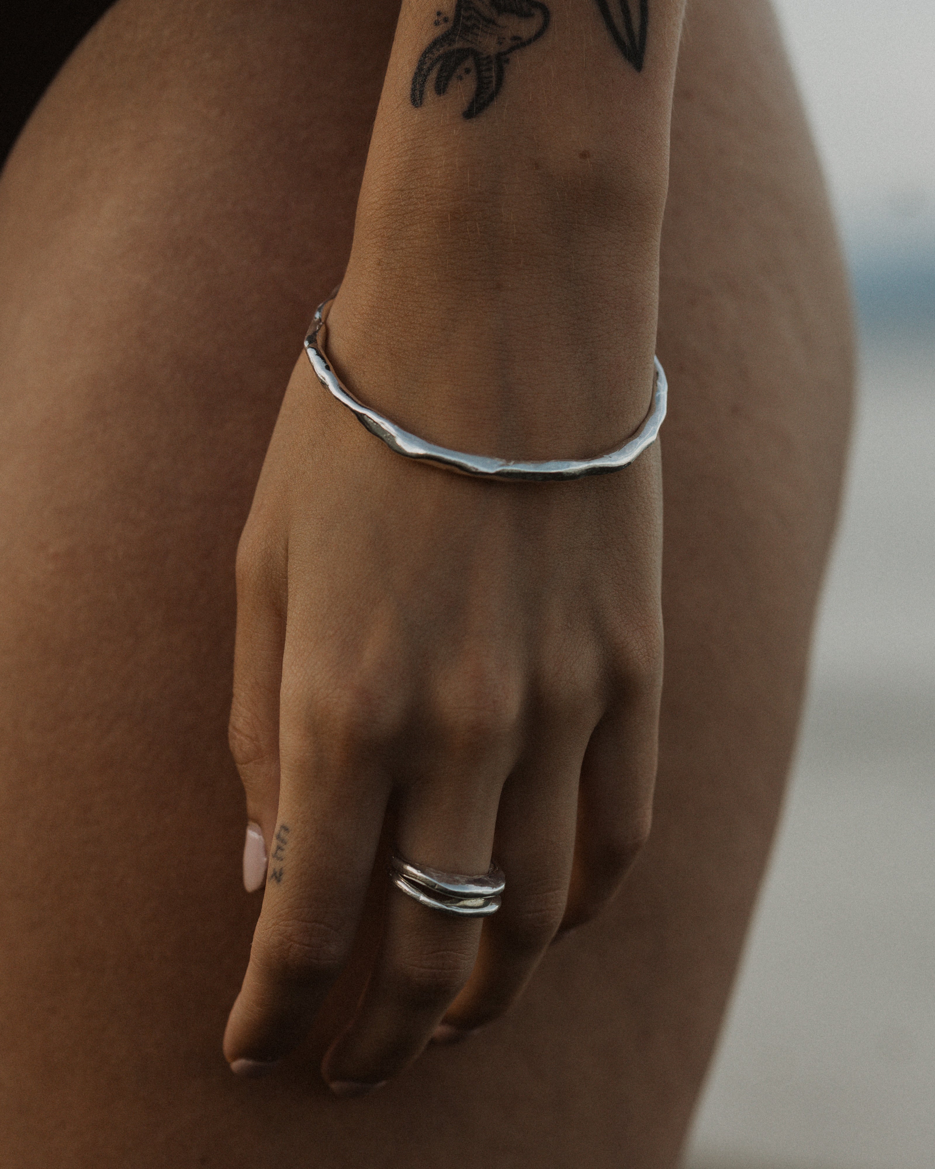 a close up of a hand and wrist wearing a stack of silver rings and a thick silver bracelet