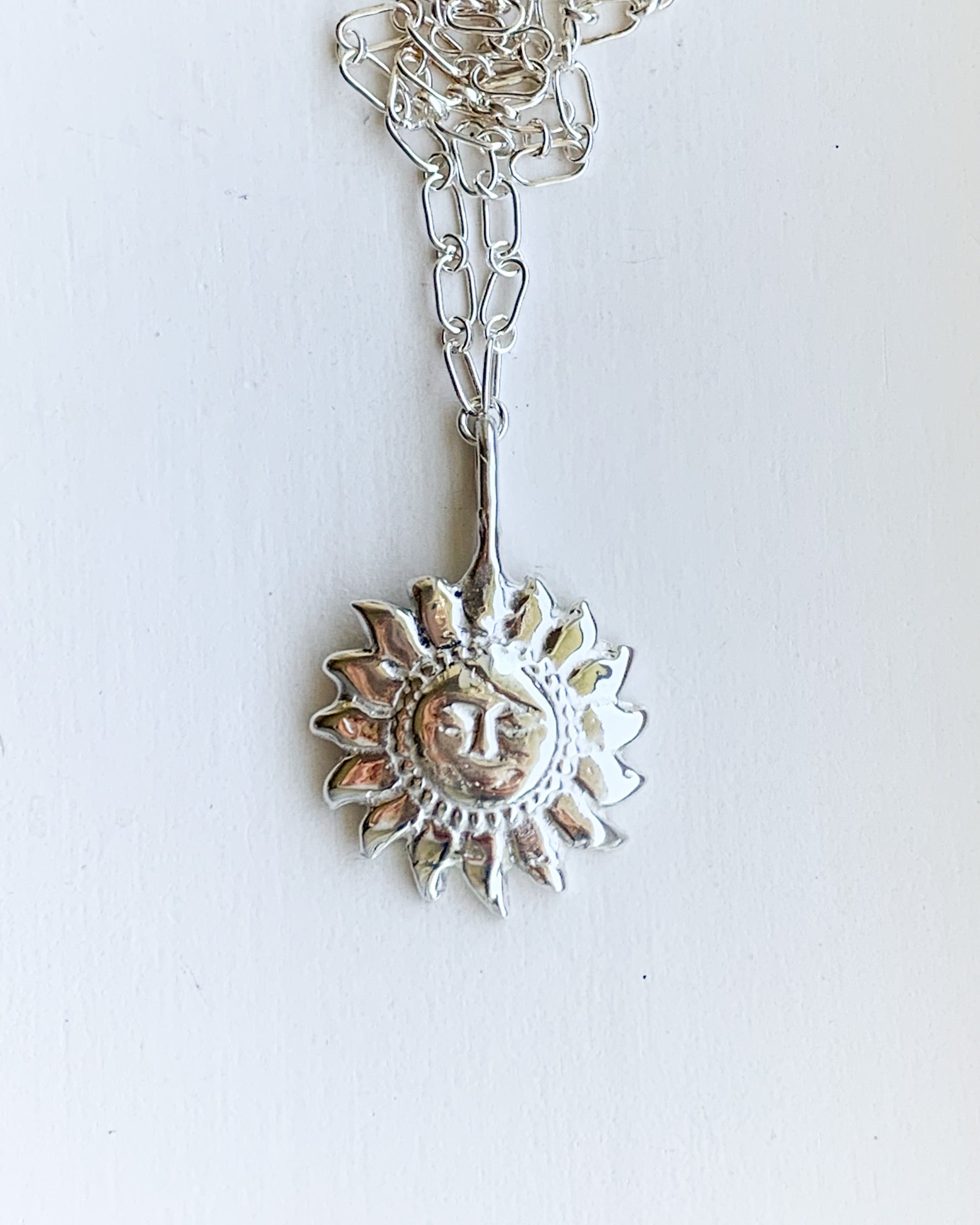a silver sun shaped pendant necklace on a silver chain, shown on a white background