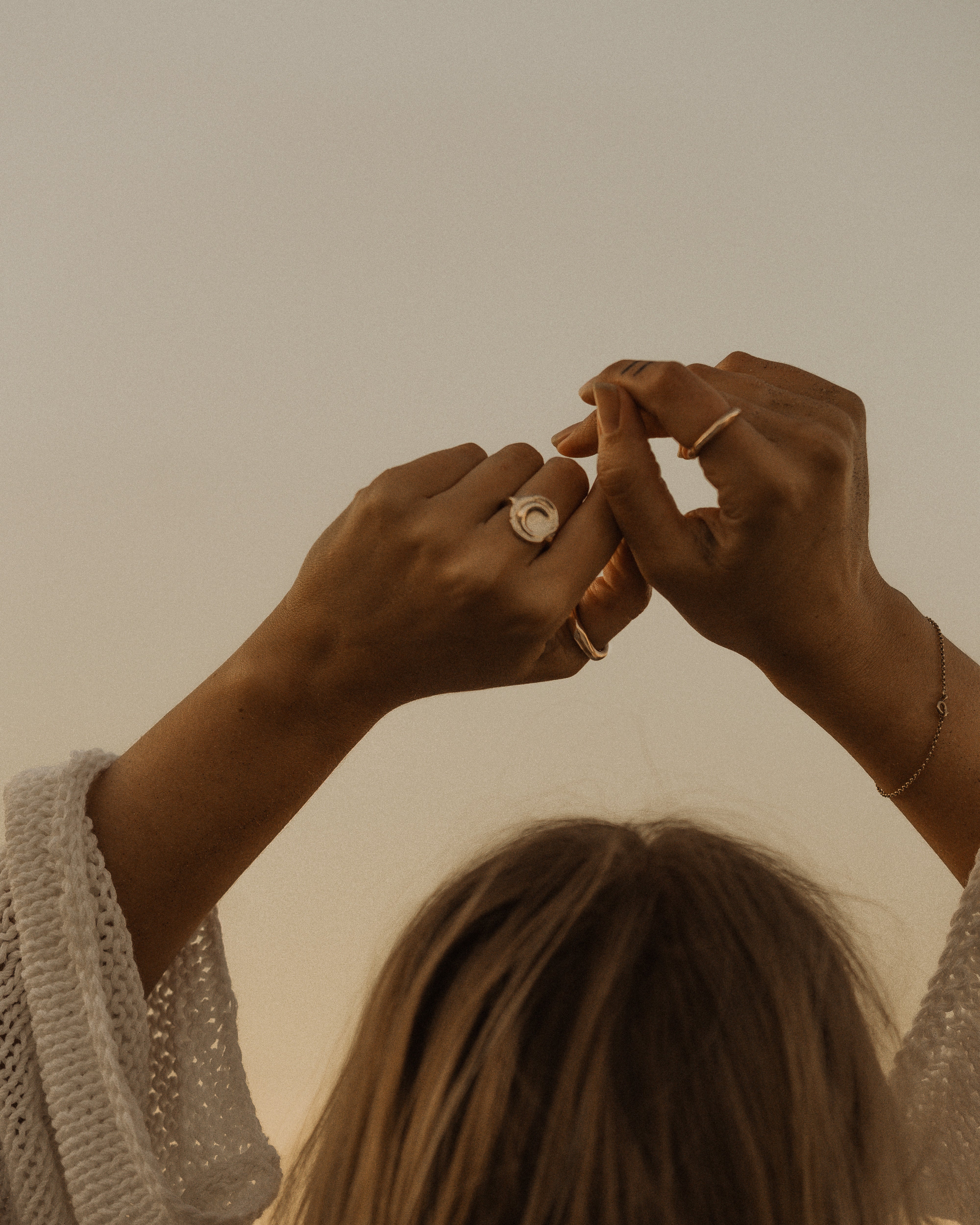 a woman holding her hands above her head against the sky with gold rings and a white knit sweater