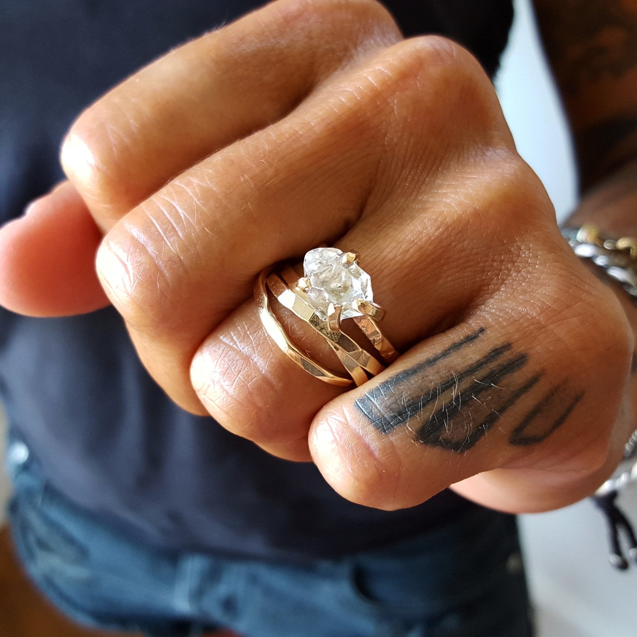 a close up of a hand with geometric finger tattoo wearing a set of intertwined band rings and claw style herkimer diamond ring