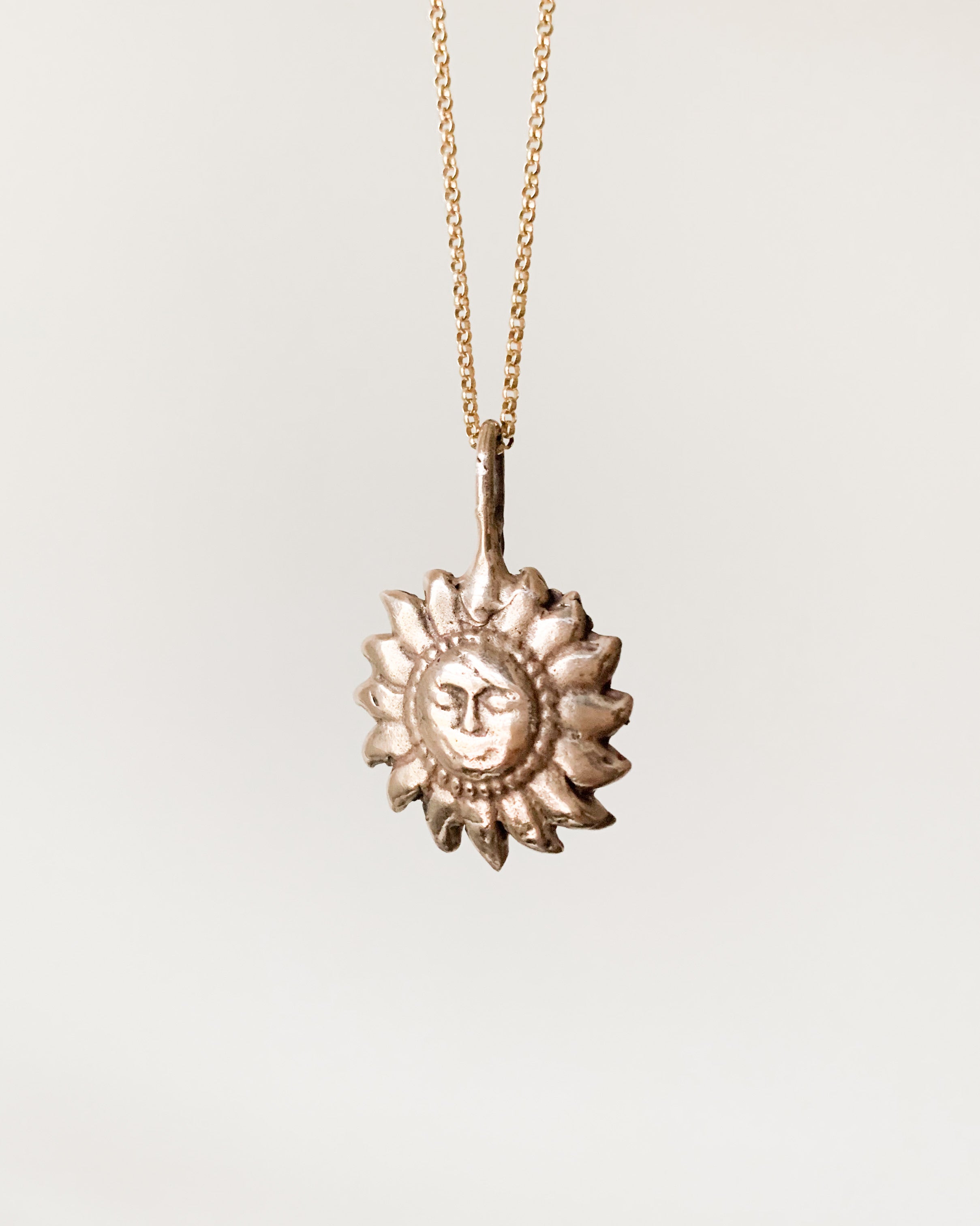 a bronze sun shaped pendant on a gold chain, shown on a white background