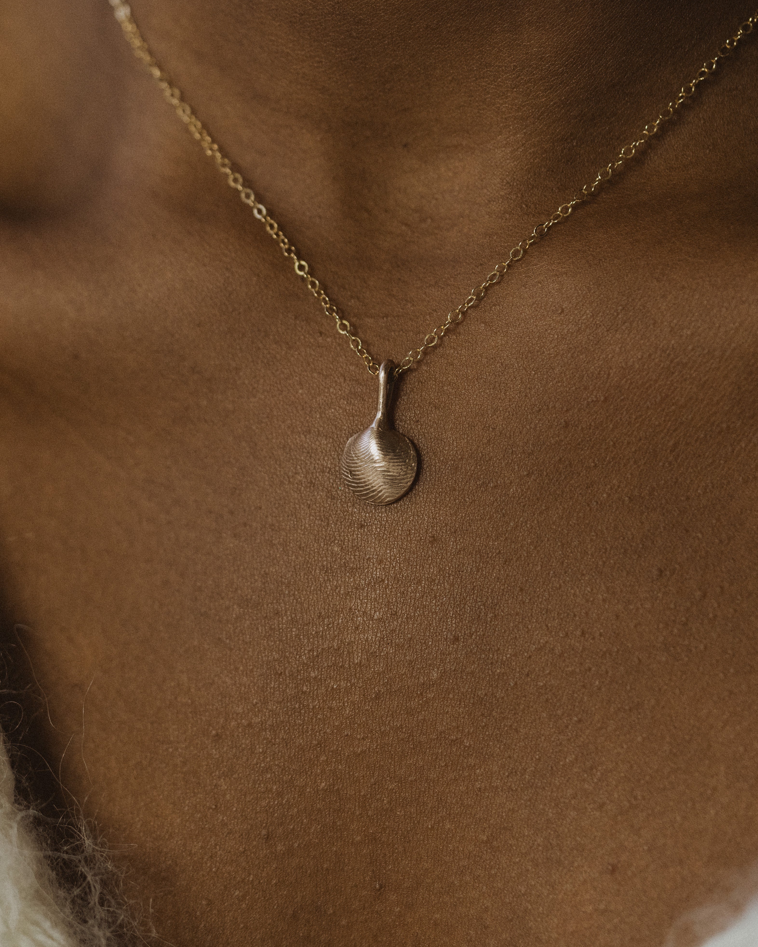 close up of a womans neck wearing a small bronze clamshell necklace